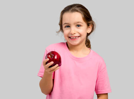 Studio portrait of a beautiful little girl holding a fresh red apple