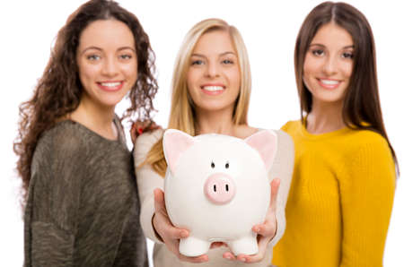 Studio portrait of three teenage girls holding a piggybankの写真素材