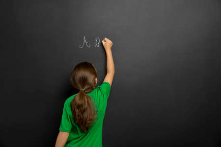 Smart little girl writing in a blackboard, with copy space