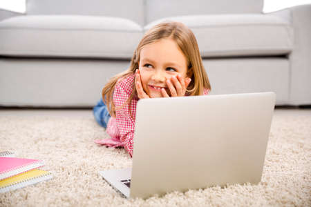 Happy little girl at home working with a laptopの写真素材