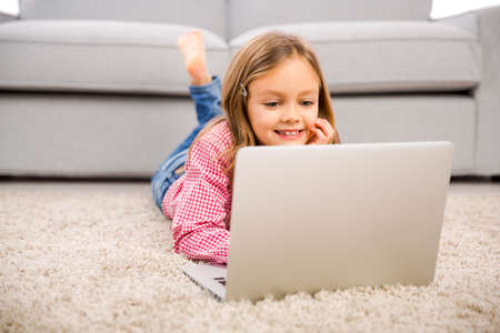 Happy little girl at home working with a laptop
