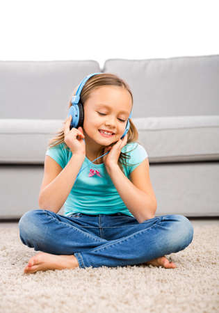 Little blonde girl at home listen music with headphonesの写真素材