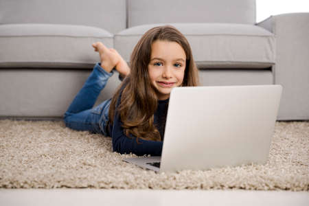 Happy little girl at home working with a laptop