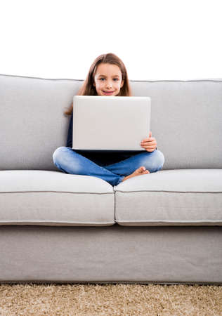 Happy little girl sitting on a couch and working a laptopの写真素材
