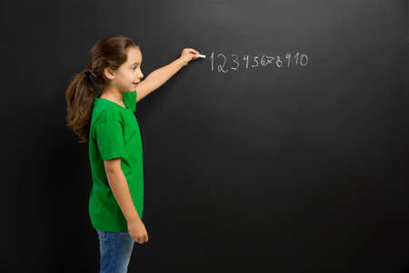 Smart little girl writing in a blackboard, with copy space