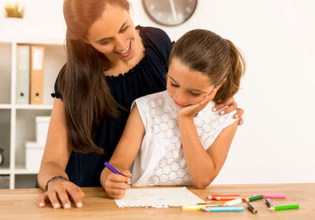 Mother helping her little daughter making drawingsの写真素材