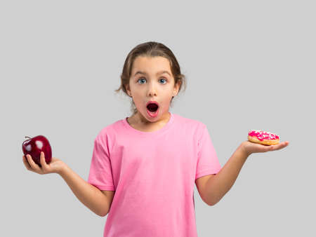 Little girl smiling and choosing between a apple and a donutの写真素材