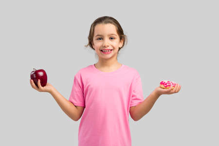 Little girl smiling and choosing between a apple and a donutの写真素材