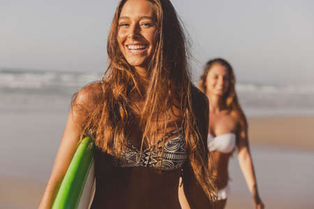 Best friends enjoying the summer, walking on the beach with a surfboardの写真素材