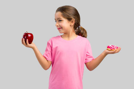 Little girl smiling and choosing between a apple and a donutの写真素材