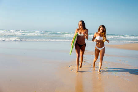 Best friends enjoying the summer, running on the beach with a surfboardの写真素材