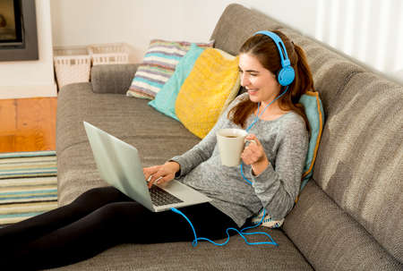 Beautiful woman working at home with a laptop while listen music and drinking coffee