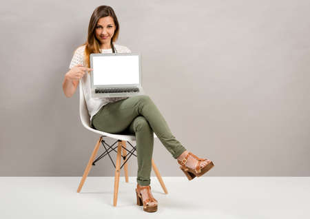 Beautiful woman sitting on a chair and showing something on a laptopの写真素材