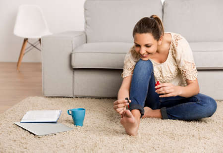 Beautiful happy woman at home making a pause to painting her nailsの写真素材