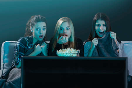 Teenage girls watching horror movie with popcornの写真素材