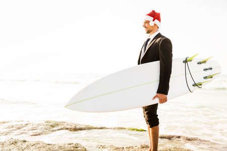 Business surfist wearing a Santa hat and holding a surfboardの写真素材
