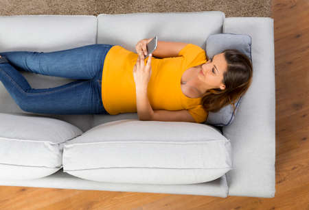 Top view of a beautiful young woman lying on a sofa and send text messagesの写真素材