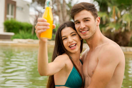 Young couple inside the pool and drinking natural juicesの写真素材