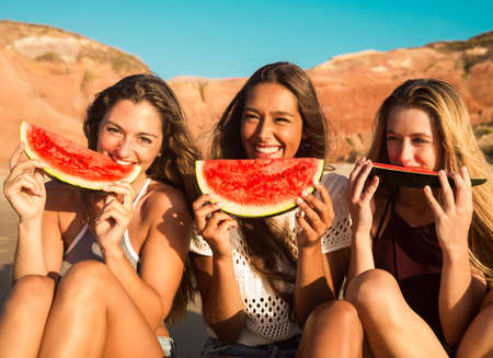 Best friends having fun on the beach and eating watermelonの写真素材