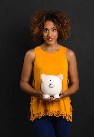 Portrait of a beautiful African American woman holding a Piggybankの写真素材
