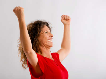 Portrait of a happy middle aged brunette with arms up expressing victoryの写真素材