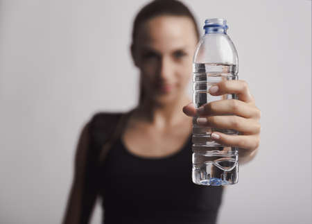 Portrait of sporty young woman holding a water bottle, against a gray background