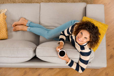 Top view of a beautiful woman on the sofa and drinking coffee