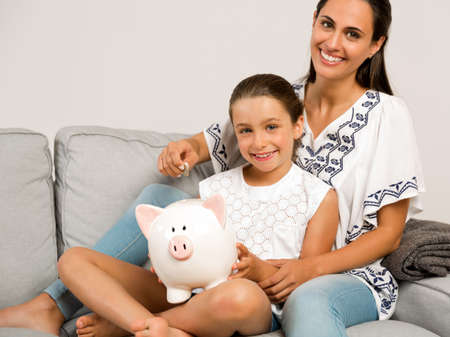 Mother and daughter putting coins into a piggy bankの写真素材
