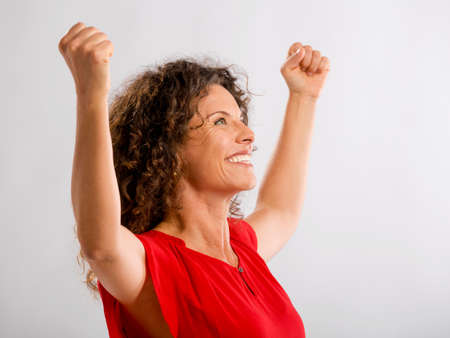 Portrait of a happy middle aged brunette with arms up expressing victory
