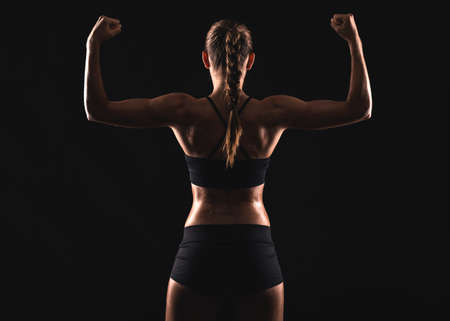 Studio shot of a fit young woman showing her muscles, against a dark backgroundの写真素材