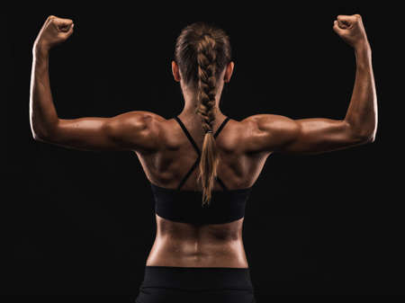 Studio shot of a fit young woman showing her muscles, against a dark backgroundの写真素材