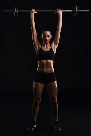 Shot of a beautiful young woman in a workout gear lifting weightsの写真素材