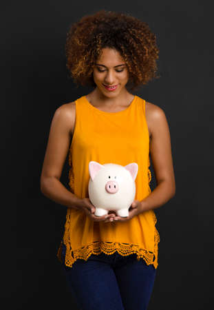 Portrait of a beautiful African American woman holding a Piggybankの写真素材