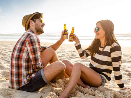 Young couple at the beach having fun, laughing and drinking beerの写真素材