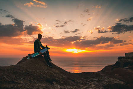 Young man with is skate board watching the sunset