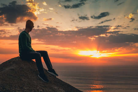Young man sitting and watching a beautiful sunsetの写真素材