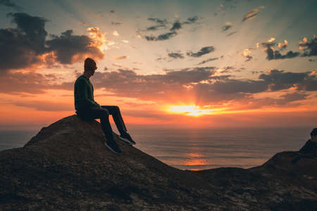 Young man sitting and watching a beautiful sunsetの写真素材