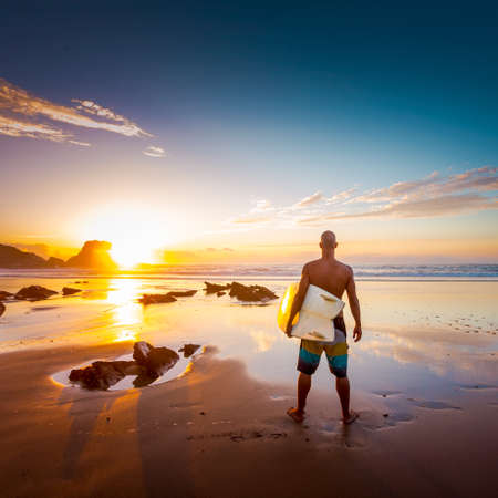 Young man on the beach with his surfboard looking at wavesの写真素材