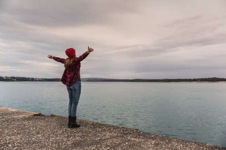 Beautiful woman standing on a pier with arms raised feeling the freedom