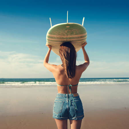 Beautiful surfer girl holding a surfboard over her head while looking to the wavesの写真素材