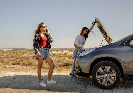 Woman near a car break down with engine trouble and her friend calls for emergency assistanceの写真素材