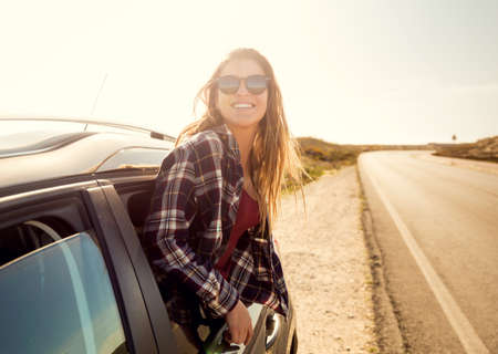 Beautiful woman looking out the car window with open arms enjoying the sunshineの写真素材
