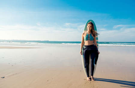 Beautiful surfer girl on the beach with her surfboard and smilingの写真素材