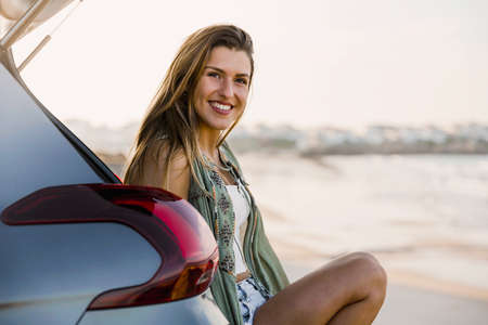 Beautiful woman sitting in the trunk of a car near a beach and smillingの写真素材