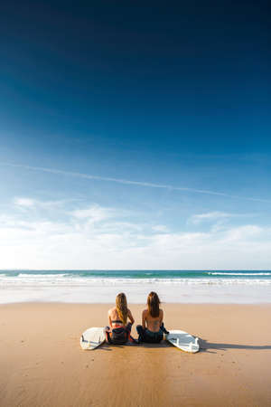 Wide view of two surfer girls on the beach with her surfboards の写真素材