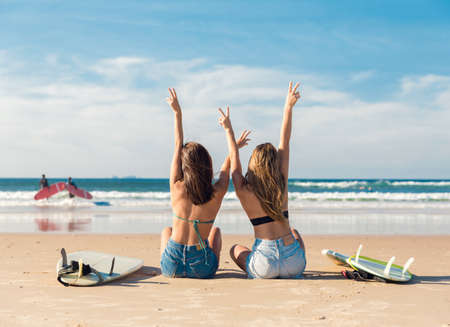 Two beautiful surfer girls at the beach with arms open