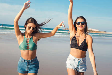 Two beautiful female friends in bikini running at the beach and having fun togetherの写真素材