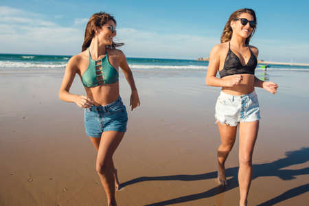 Two beautiful female friends in bikini running at the beach and having fun togetherの写真素材