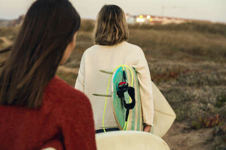 Two female surfers walking near the coastline with surfboardsの写真素材