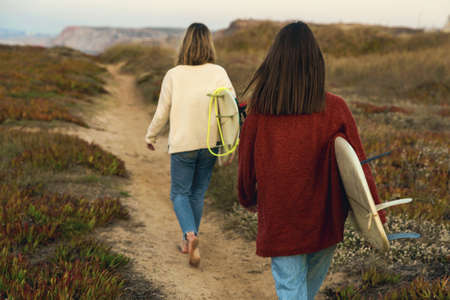 Two female surfers walking near the coastline with surfboardsの写真素材